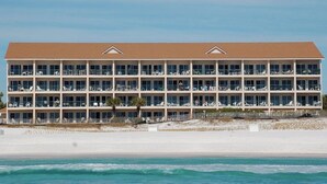 Hotel de varios pisos con balcones, situado cerca de una playa con arena y olas del océano.