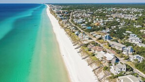 Vista aérea de una zona residencial costera con casas a lo largo de la playa, agua azul cristalina y cielo despejado.