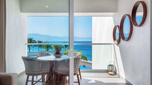 Enjoy a panoramic ocean view from this room's large window, featuring a round dining table, potted plant, and comfortable seating for four.