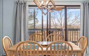 Un comedor con una mesa y sillas de madera, una araña y vistas amplias por ventanas grandes.