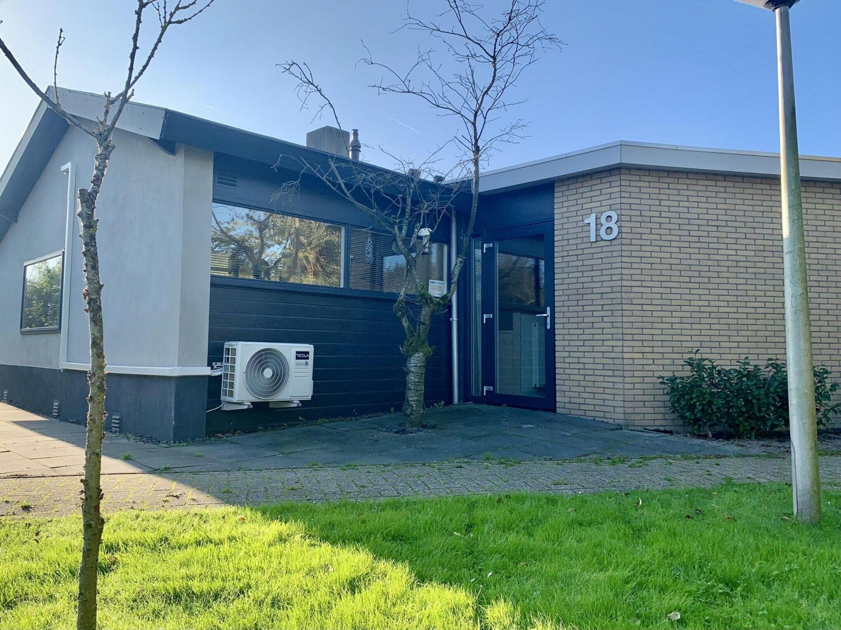 Un edificio moderno con un equipo de aire acondicionado Tesla, una sección de ladrillo y un letrero con el número 18.