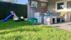 A patio area with a wooden bench, cushions, and a children's slide. - Bungalow in Sint Maartenszee With Veranda (Sint Maartensvlotbrug)