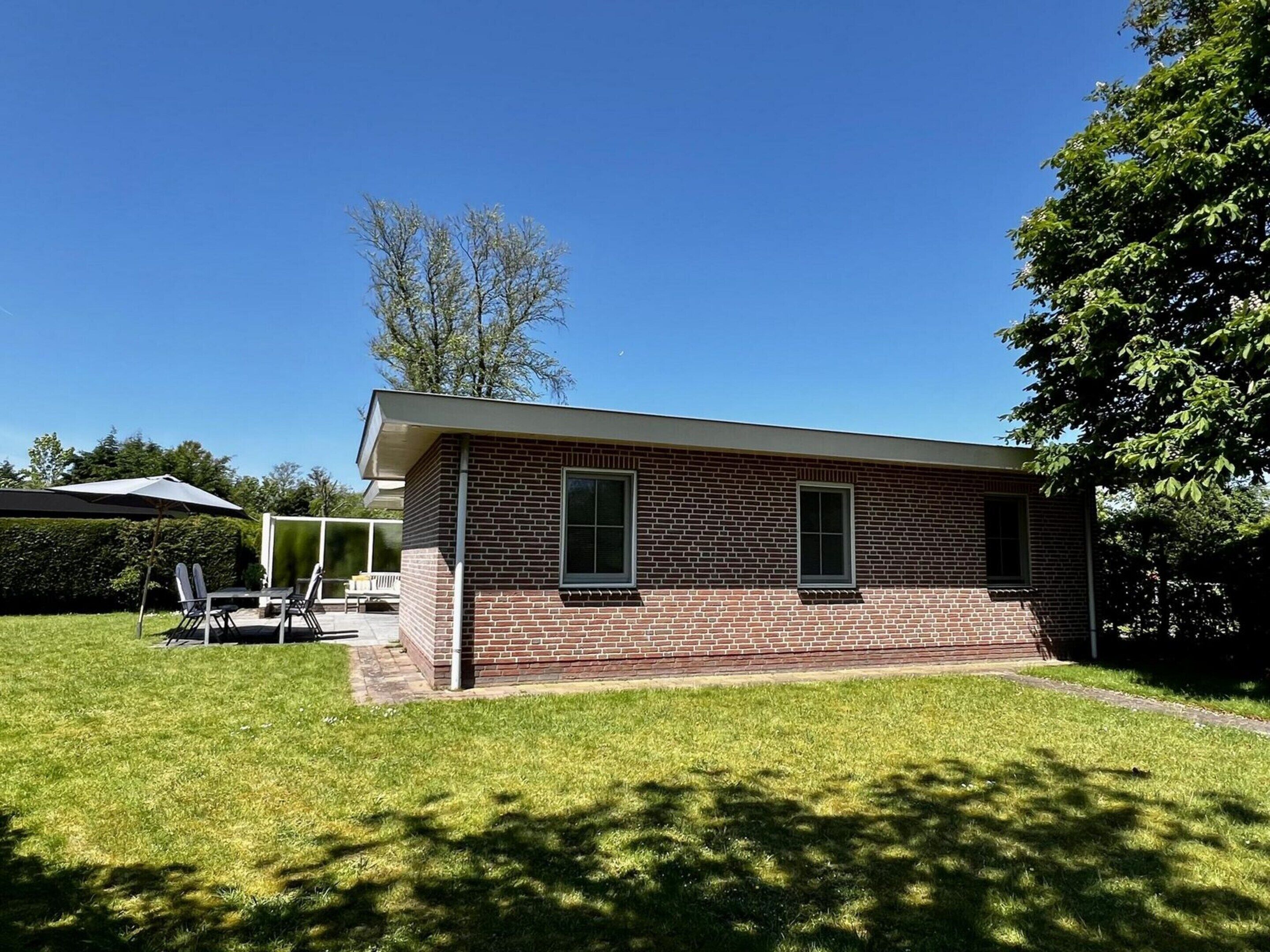A single-story brick house with a flat roof, a small porch, and a well-maintained lawn.