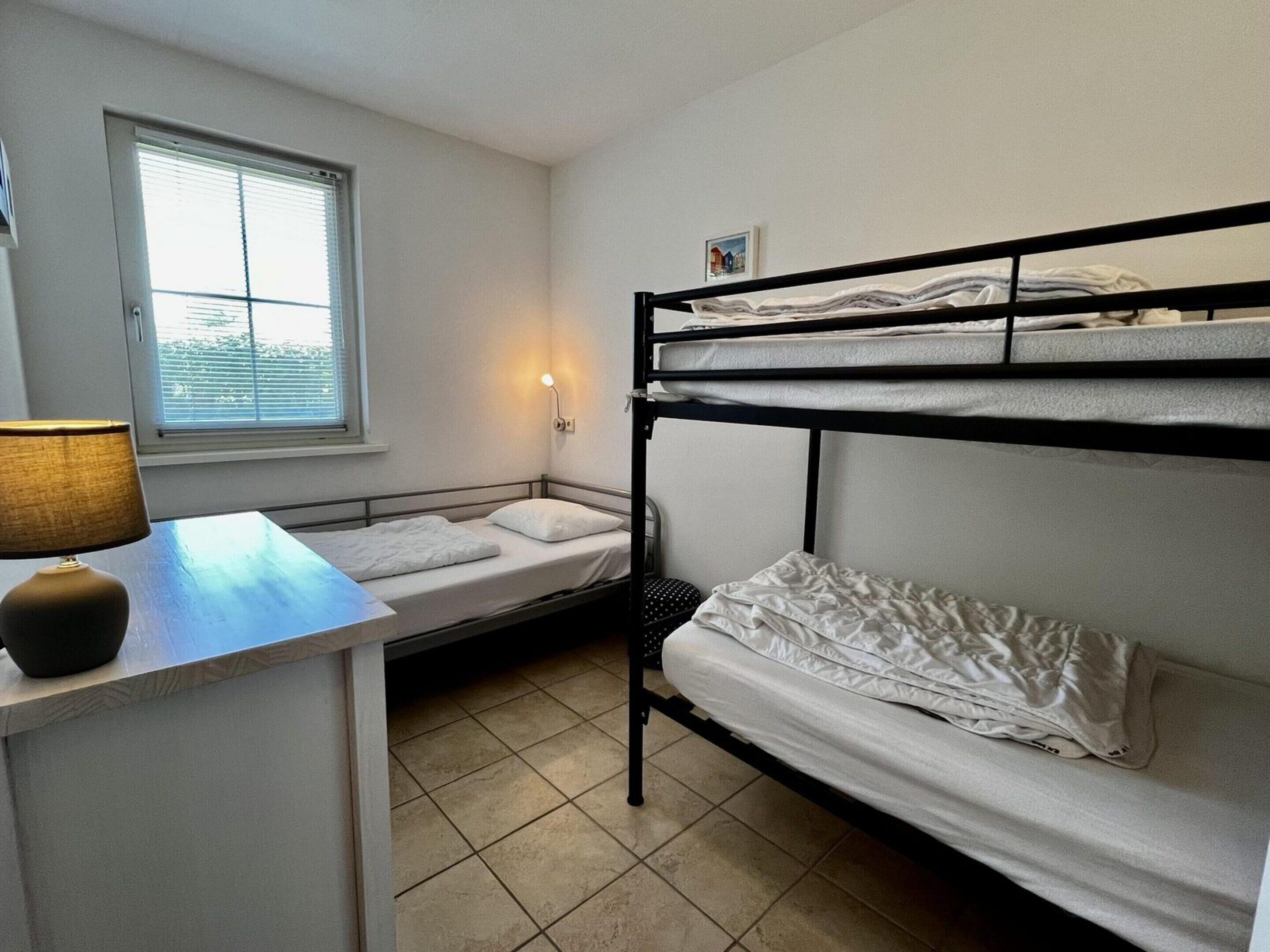 Habitación con literas, escritorio, lámpara, ventana con persianas y luz en la pared.