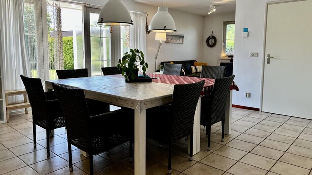 Un coin repas avec une table et des chaises, une plante en pot et une vue sur l’extérieur grâce à de grandes fenêtres.