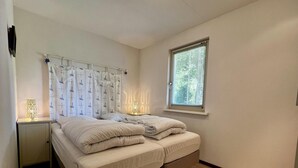 Une chambre à coucher comprenant un lit, une table de chevet, une fenêtre avec des stores et un luminaire fixé au mur.