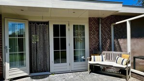 Un patio couvert comprenant un banc, une porte-fenêtre coulissante et un mur en briques.