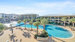 A resort with a large swimming pool, palm trees, and a multi-story building with balconies. - Adagio D-103 Poolside 3/3 - NEW to program for 2025! (Santa Rosa Beach)