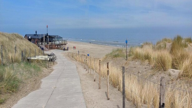 A coastal walkway leading to a beach with a lifeguard station and a building with a glass enclosure. - Cosy Holiday Home Near Beach (Sint Maartensvlotbrug)
