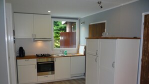 A compact kitchen with white cabinets, a wooden countertop, a gas stove, and a built-in oven. - Cosy Holiday Home Near Beach (Sint Maartensvlotbrug)