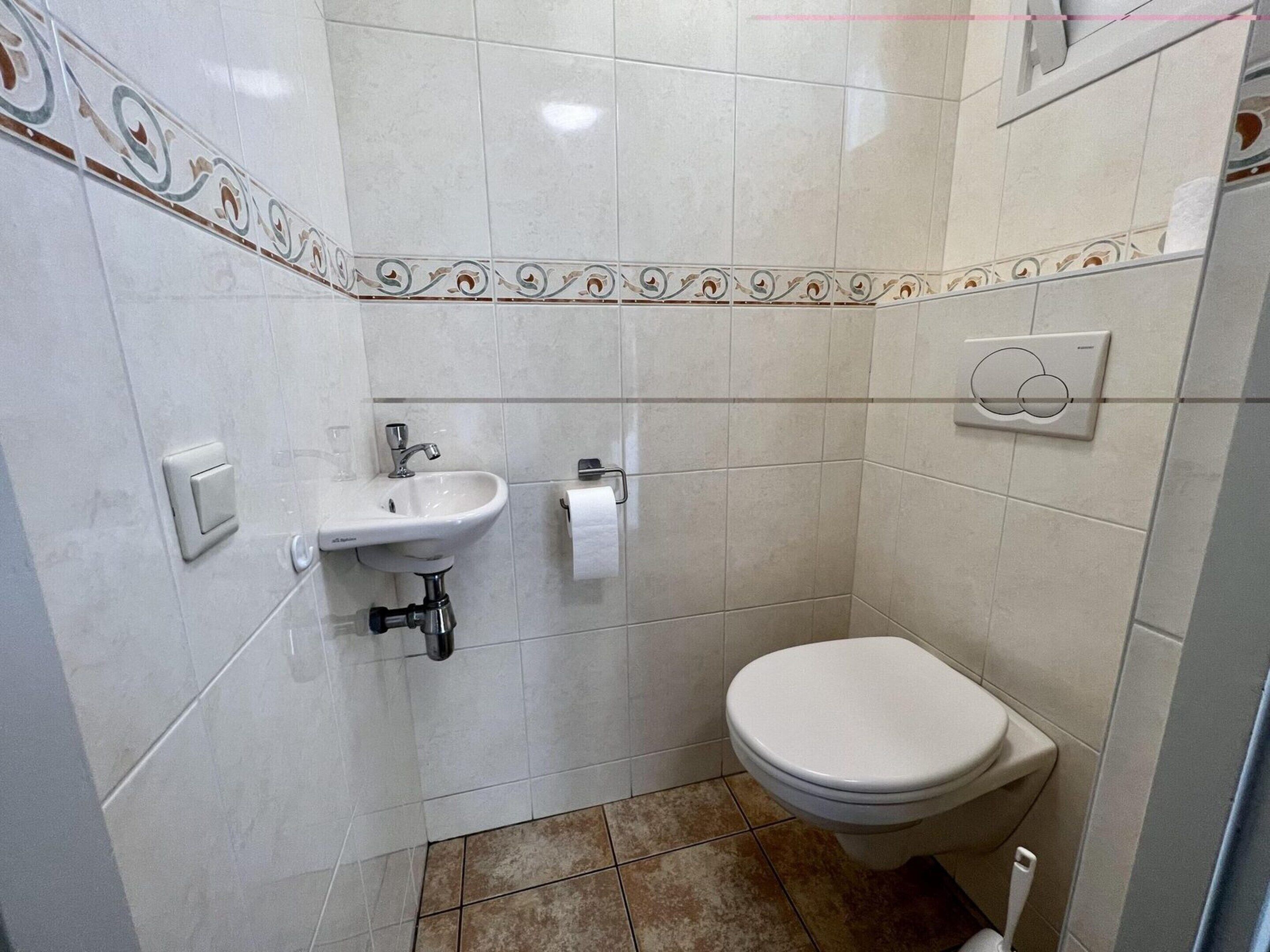 Ein kleines Badezimmer mit einem weißen Waschbecken, einer Toilette und einem Handtuchspender.