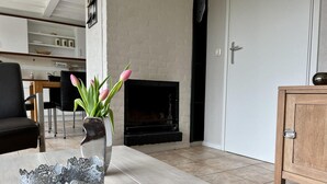 A modern living room with a fireplace, a dining area in the background, and a wooden cabinet. - Detached Holiday Home With Garden (Sint Maartensvlotbrug)