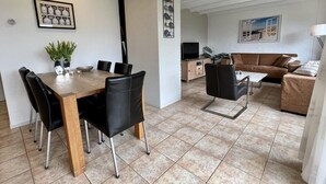 A modern living room with a wooden dining table, black chairs, a brown sofa, and a TV. - Detached Holiday Home With Garden (Sint Maartensvlotbrug)