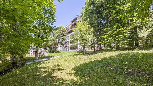 A grassy area with trees and a building with multiple floors and balconies.
