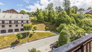 A building with multiple balconies, a road in front, and a wooded hillside.