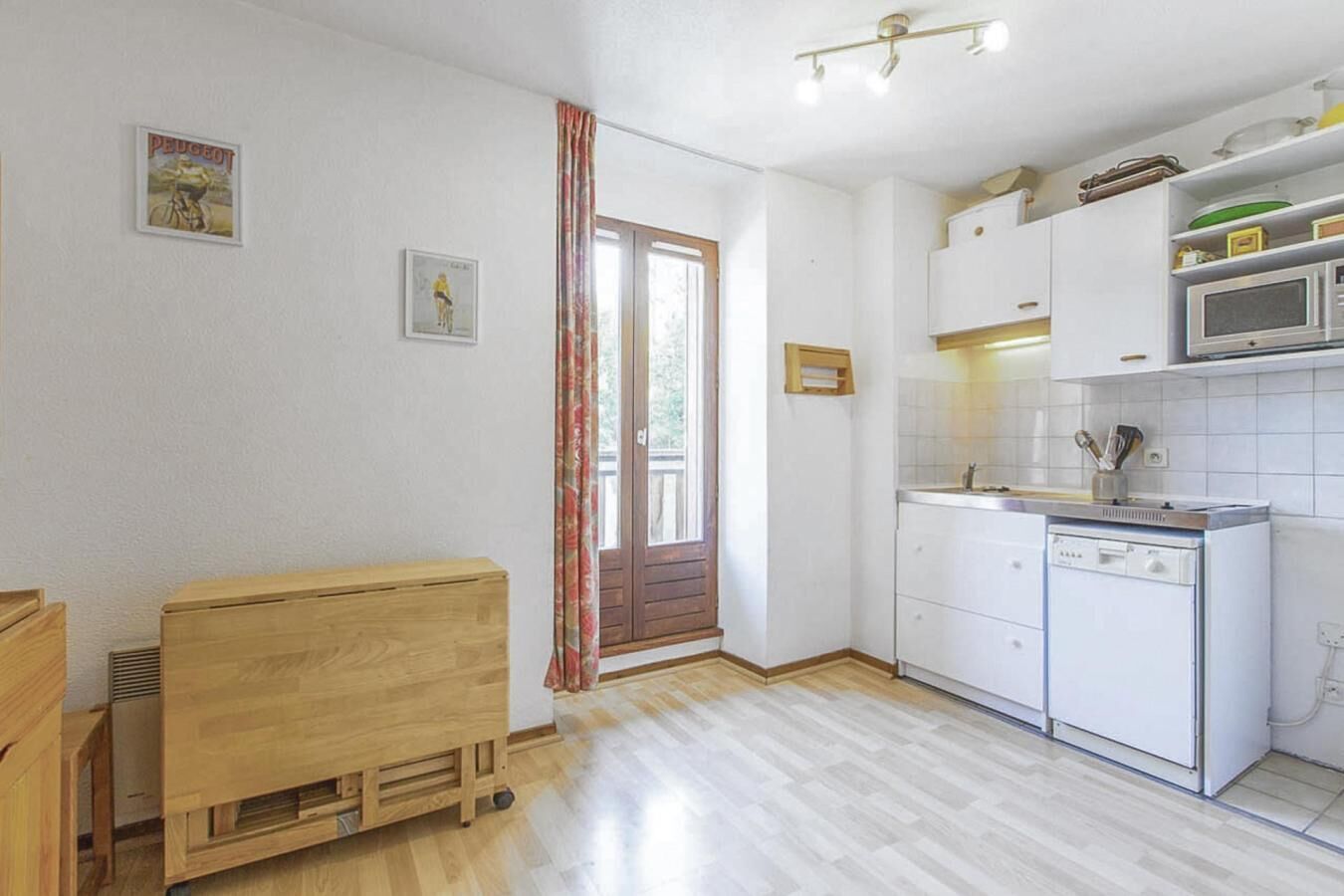 Una cocina funcional con armarios blancos, microondas y lavavajillas. Incluye una banca de madera y un ventanal con cortina.