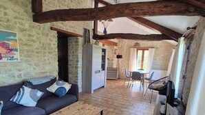 Un ambiente rustico con divano, tavolino in legno, pareti in pietra, travi a vista e angolo cottura.