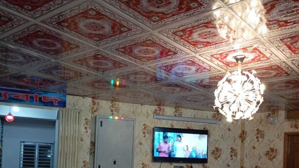 A room with a patterned ceiling, a television mounted on the wall, a sofa, and a decorative chandelier. - Hotel Moon International  (Dhaka)