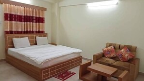 A bedroom with a wooden bed, a wooden nightstand, a wooden chair with cushions, and a red rug. - Hotel Moon International  (Dhaka)