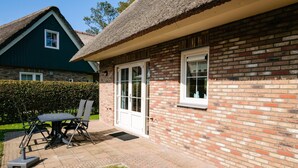 A house with a brick exterior, a thatched roof, and a patio with a table and chairs. - Villa Close to Forest, Beach & sea (Sint Maartensvlotbrug)