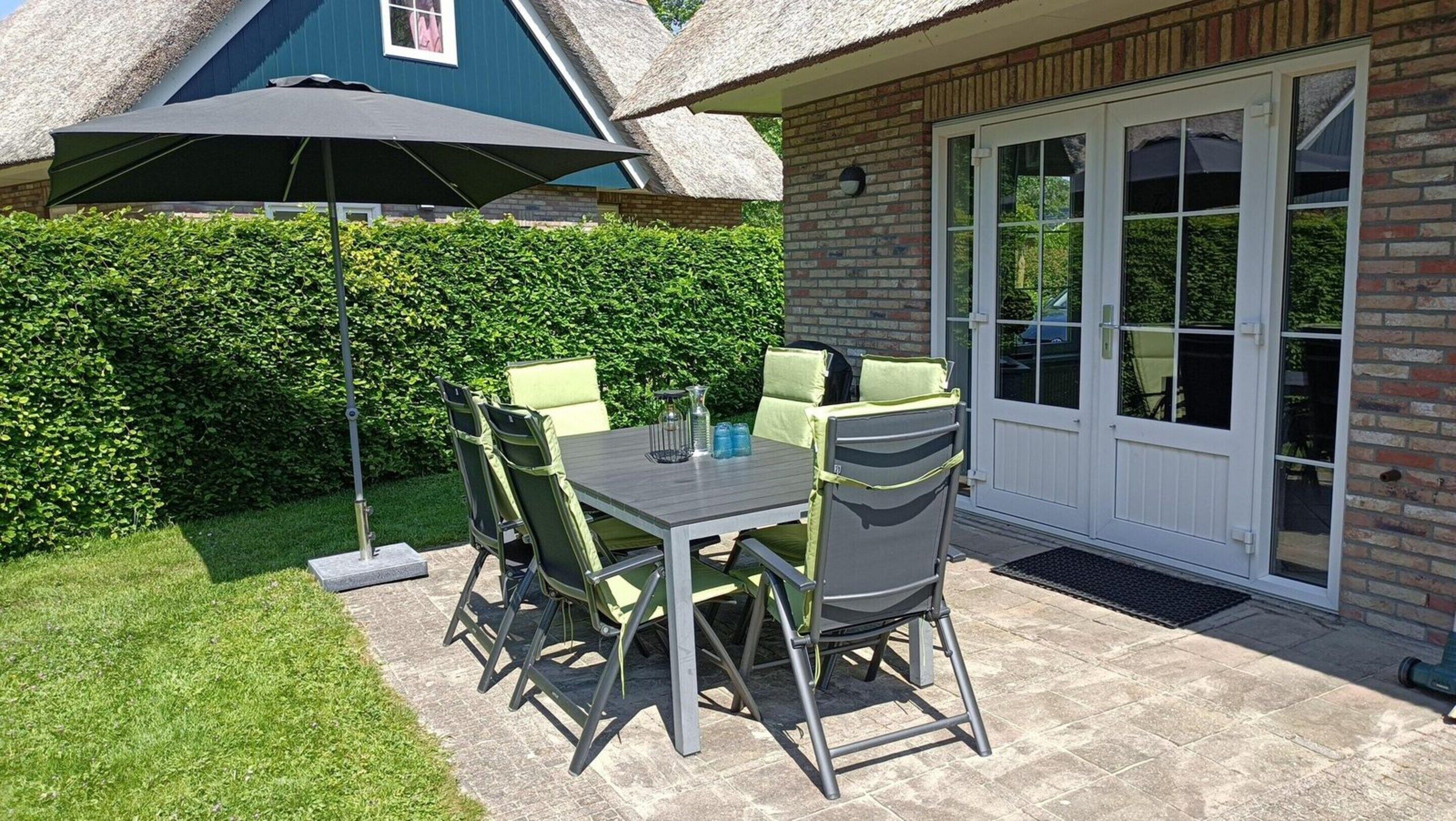 A patio with a table and chairs, a large umbrella, and a door leading to a covered area.
