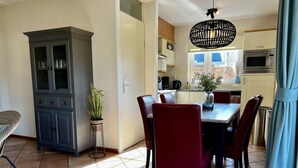 A dining area with a table and chairs, a cabinet, a potted plant, and a hanging light fixture. - Villa Close to Forest, Beach & sea (Sint Maartensvlotbrug)