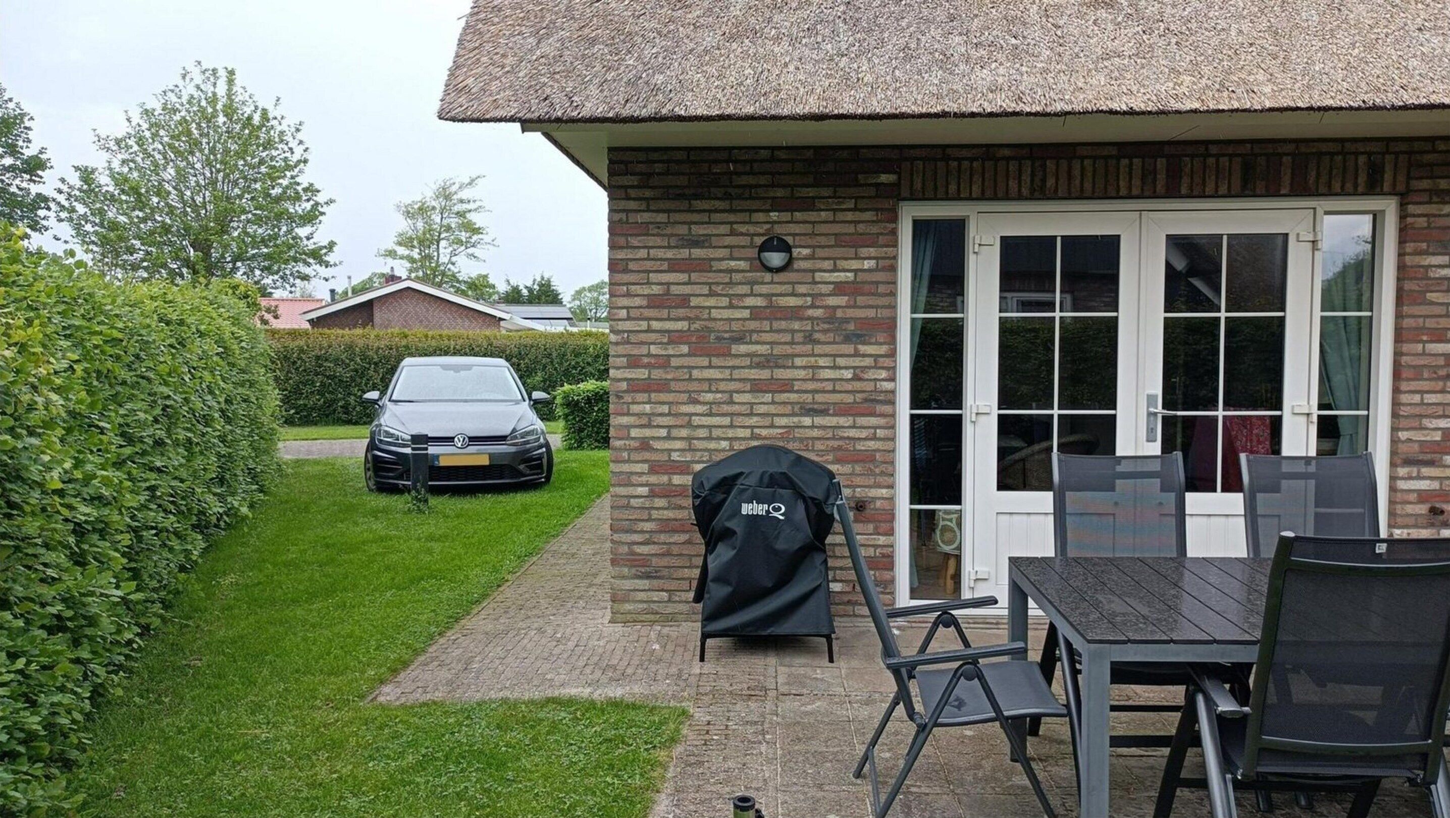 A house with a brick exterior, a thatched roof, and a patio area with a grill and outdoor furniture.