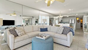A modern living room with a sectional sofa, ottoman, and a flat-screen TV. - ASHWORTH OCEAN FRONT (NORTH MYRTLE BEACH)