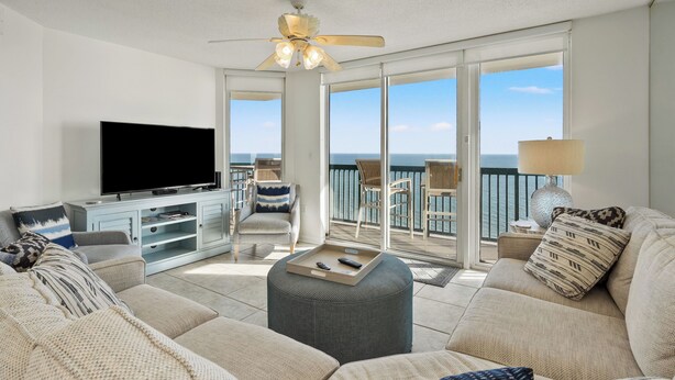 A spacious living room with a flat-screen TV, comfortable seating, a ceiling fan, and a balcony with a view of the ocean. - ASHWORTH OCEAN FRONT (NORTH MYRTLE BEACH)