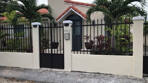 A gated property with a numbered address sign, a tiled roof, and surrounding greenery.