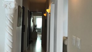 A hallway with white columns, wall sconces, and a tiled floor.