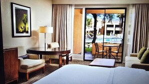 Habitación de hotel con cama, escritorio, silla, sofá y vistas a una piscina y un edificio.