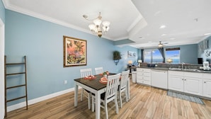 Un comedor con mesa y sillas de madera, una cocina con armarios blancos y vista al océano.