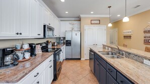 A kitchen with white cabinets, a stainless steel refrigerator, a double sink, and a coffee maker. - Walk to Beach | 4BR Sleeps 14 | Pool | Pet Friendly | Near Pier Park (Panama City Beach)