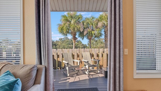 Vista desde una habitación a una terraza exterior con valla de madera, una mesa y sillas.
