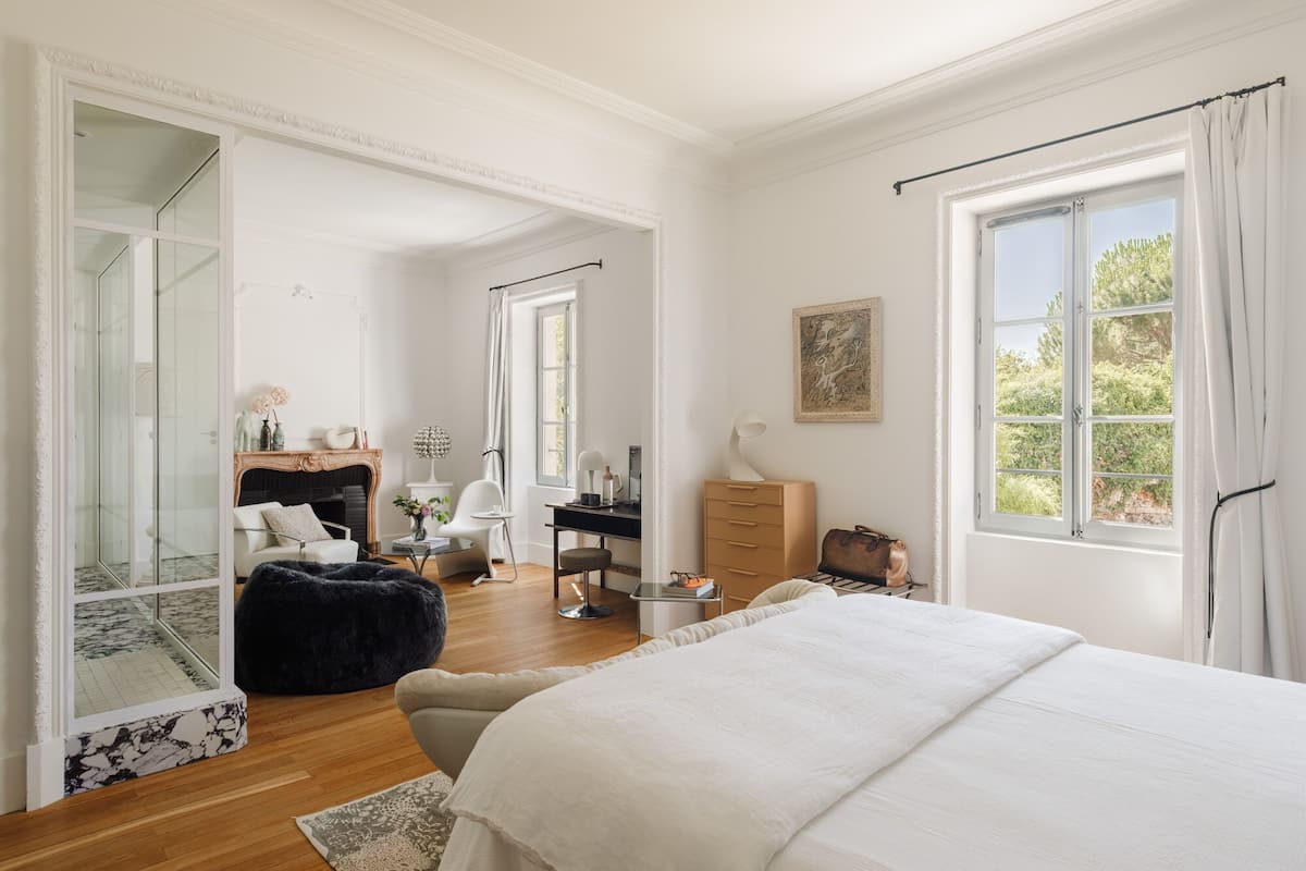 Un dormitorio amplio con una cama grande, un escritorio y una silla. Hay un armario, un espejo y una ventana con cortinas.