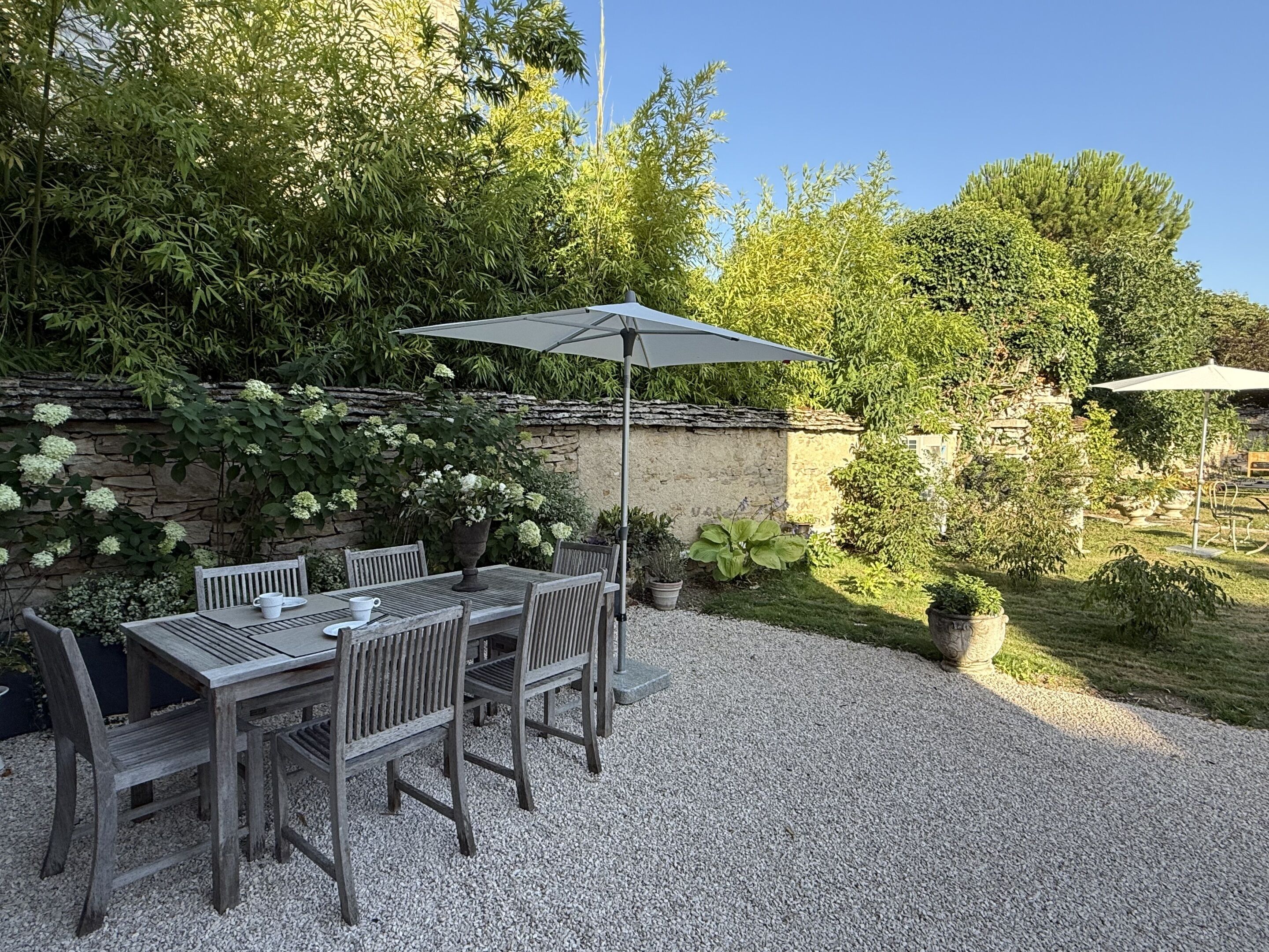 Eine Terrasse mit Holztisch und Stühlen, einem großen Sonnenschirm und einer Steinmauer mit Grünpflanzen.