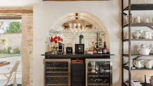 A kitchen with a wine fridge, shelves with glassware, and a view of the garden.