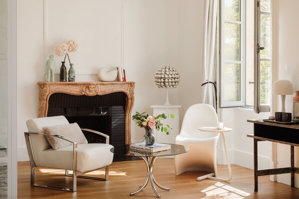 A living room with a fireplace, a white armchair, a glass coffee table, and a modern lamp. - La Cour de Beaune (Beaune)