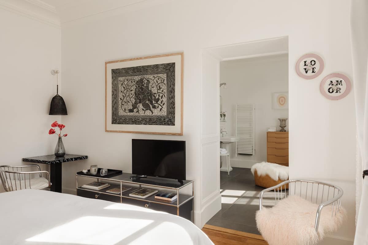Un dormitorio moderno con una cama, un televisor, un escritorio con lámpara y una obra de arte enmarcada en la pared.
