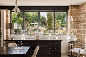 A modern dining area with a view of a garden through large windows, a black dining table with a wine glass, and a white chair. - La Cour de Beaune (Beaune)