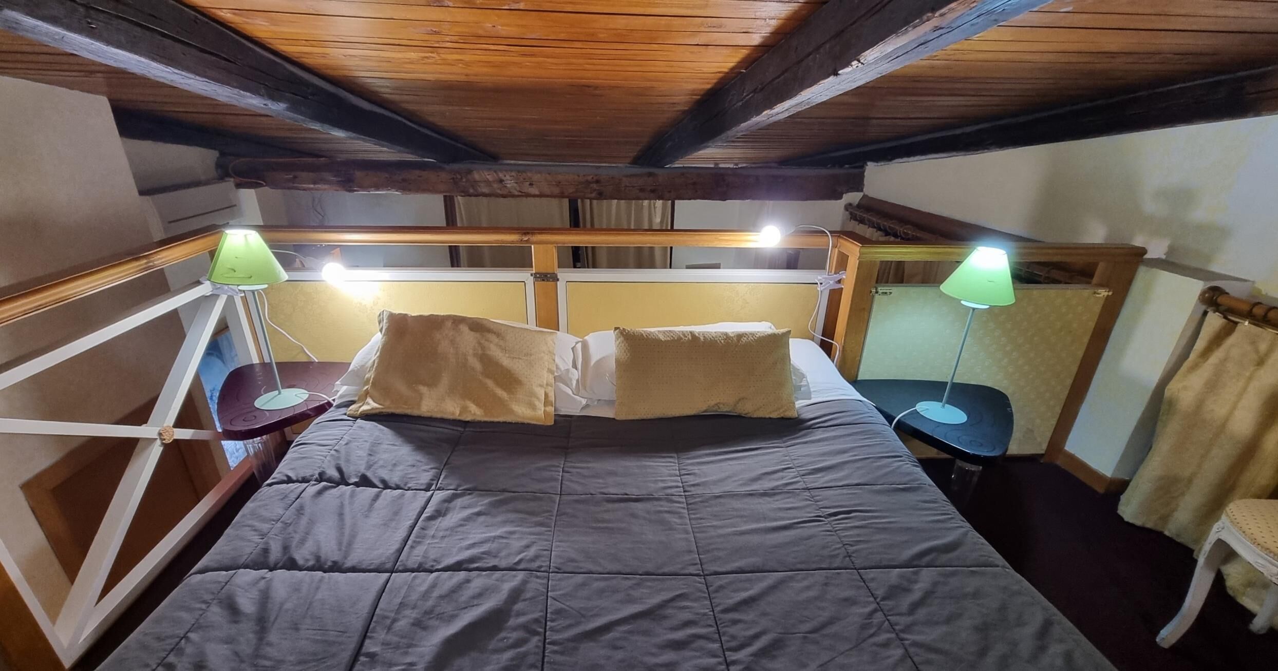 A room with a bed, two bedside tables with lamps, a window, and wooden beams on the ceiling.