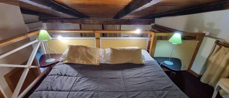 A room with a bed, two bedside tables with lamps, a window, and wooden beams on the ceiling.