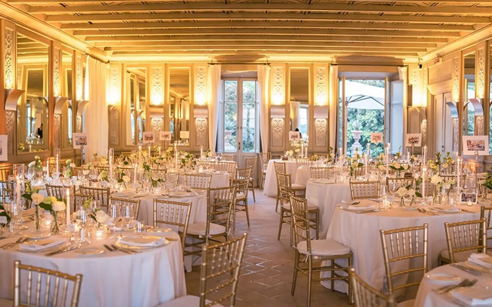 A banquet hall with round tables, gold chairs, and white tablecloths.