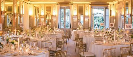 A banquet hall with round tables, gold chairs, and white tablecloths.