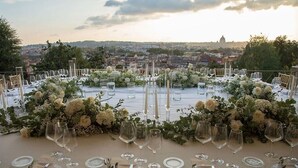 Een ronde tafel gedekt voor een formeel evenement, met een stadsgezicht op de achtergrond.