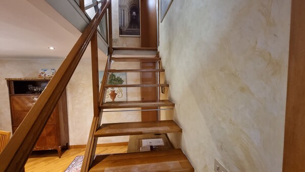 Una escalera de madera que lleva a un rellano con vistas a un pasillo y una zona de cocina.