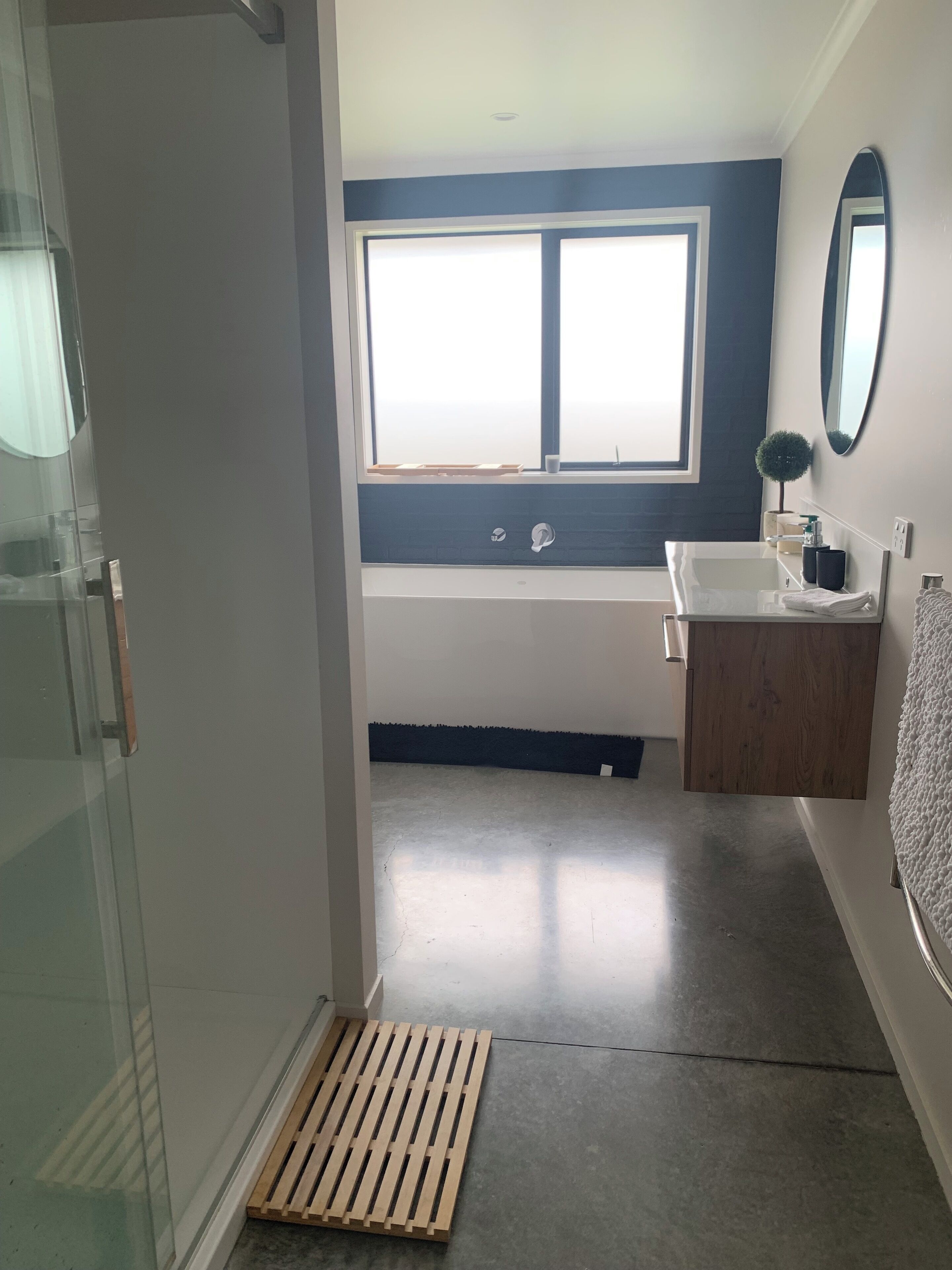 A modern bathroom with a glass shower enclosure, a large window, a bathtub, and a wooden vanity.