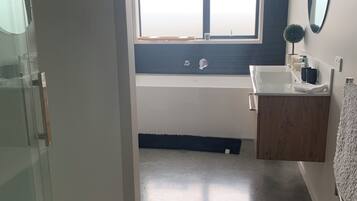 A modern bathroom with a glass shower enclosure, a large window, a bathtub, and a wooden vanity.
