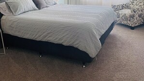 A neatly arranged bedroom with a large bed, a chair, and a window with sheer curtains. - Modern & Spacious 2yo Home (New Plymouth)